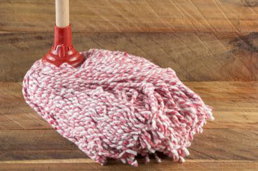 Cleaning an unfinished wood floor with a mop dipped in vinegar.