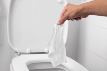 Woman throwing wet baby wipes into the toilet.
