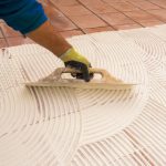 Man applying tile adhesive over old tiles to install a new layer of tile.