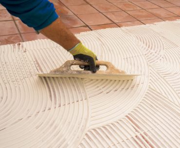 Man applying tile adhesive over old tiles to install a new layer of tile.