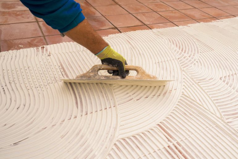 Man applying tile adhesive over old tiles to install a new layer of tile.
