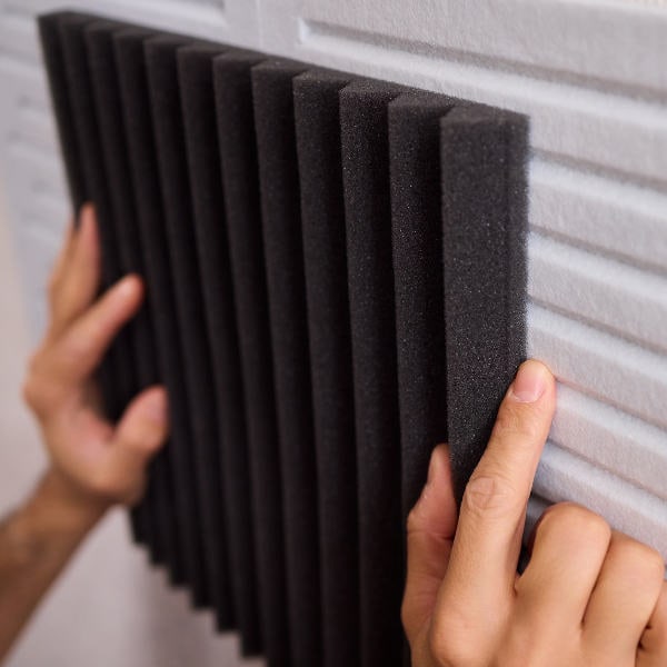 Installing a black acoustic foam panel on a wall.