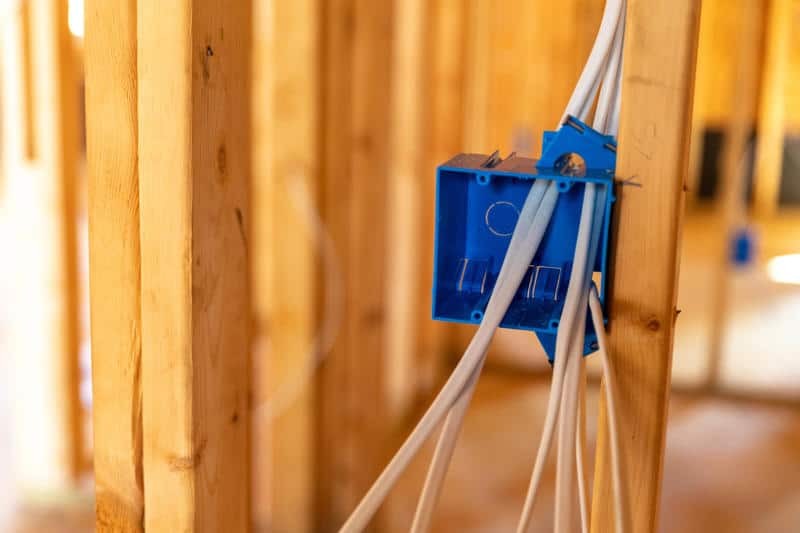 An unfinished house interior showing exposed wall studs and newly installed electrical cables and outlet boxes.