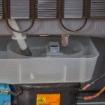 Rear view of a refrigerator showing the compressor and the area where refrigerant lines and service ports are located.