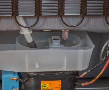 Rear view of a refrigerator showing the compressor and the area where refrigerant lines and service ports are located.