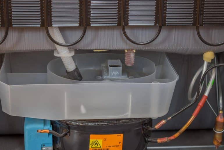Rear view of a refrigerator showing the compressor and the area where refrigerant lines and service ports are located.