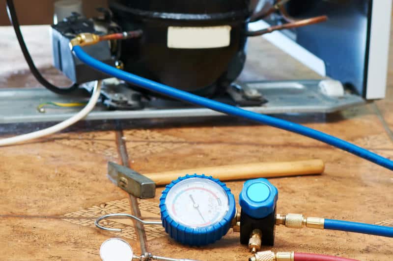 Connecting gauges and a refrigerant tank to the back of a refrigerator to service the cooling system.