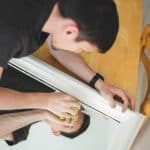 A man carefully cleaning and polishing a scratched mirror surface to reduce visible marks and restore clarity.
