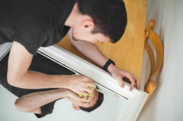 A man carefully cleaning and polishing a scratched mirror surface to reduce visible marks and restore clarity.