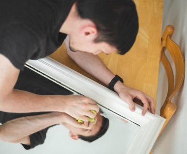 A man carefully cleaning and polishing a scratched mirror surface to reduce visible marks and restore clarity.