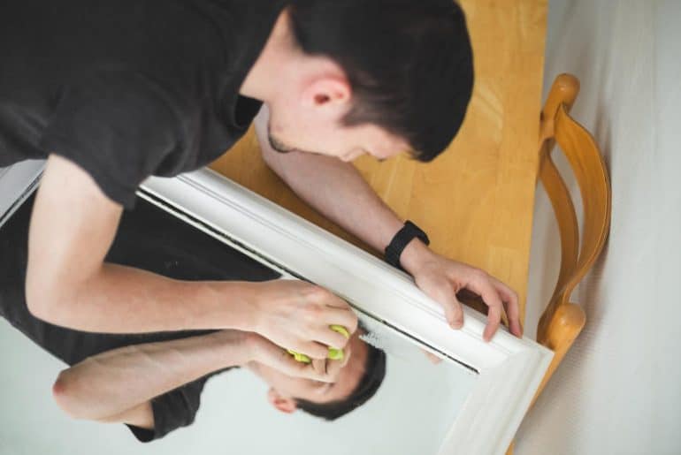 A man carefully cleaning and polishing a scratched mirror surface to reduce visible marks and restore clarity.