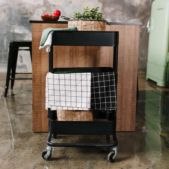 A slim rolling cart beside a kitchen island holding towels and everyday essentials, adding flexible, movable storage in a small kitchen.