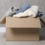 Clothing piled inside a cardboard box placed directly on the floor, showing a common storage mistake.