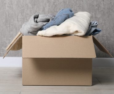 Clothing piled inside a cardboard box placed directly on the floor, showing a common storage mistake.