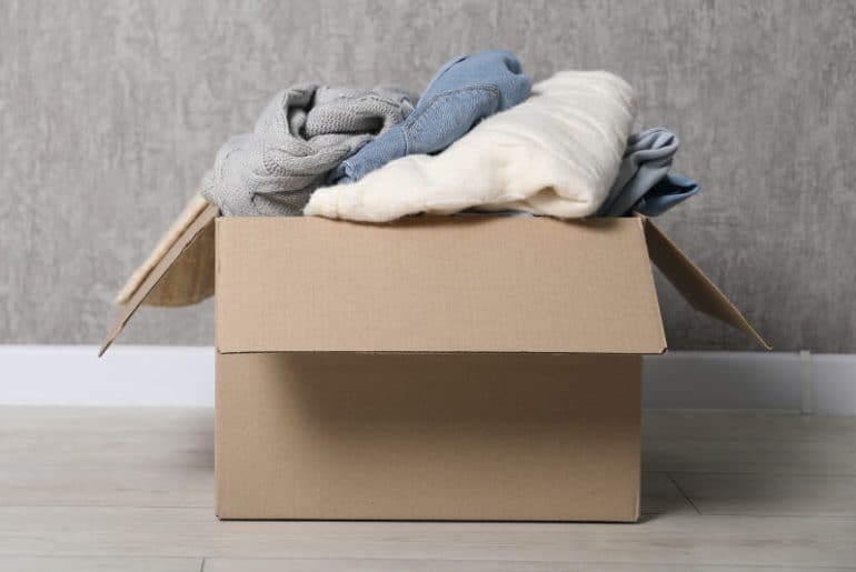 Clothing piled inside a cardboard box placed directly on the floor, showing a common storage mistake.