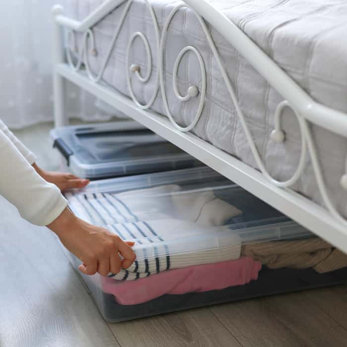 Clear storage bins filled with neatly folded clothes tucked under a bed.